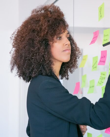 Mulher escrevendo em post-its coloridos fixados em um quadro de vidro, organizando metas com foco na aplicação da metodologia SMART.