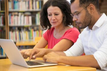 Dois estudantes analisando informações no notebook e tirando dúvidas sobre pós-graduação lato sensu e stricto sensu.