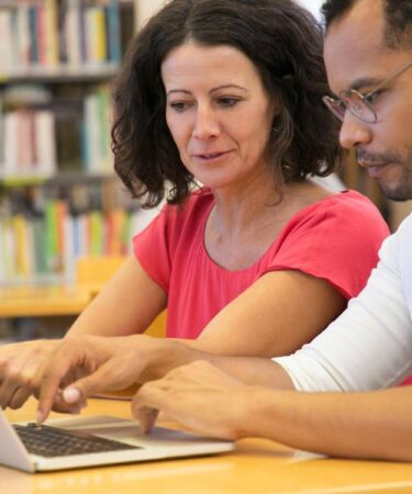 Dois estudantes analisando informações no notebook e tirando dúvidas sobre pós-graduação lato sensu e stricto sensu.