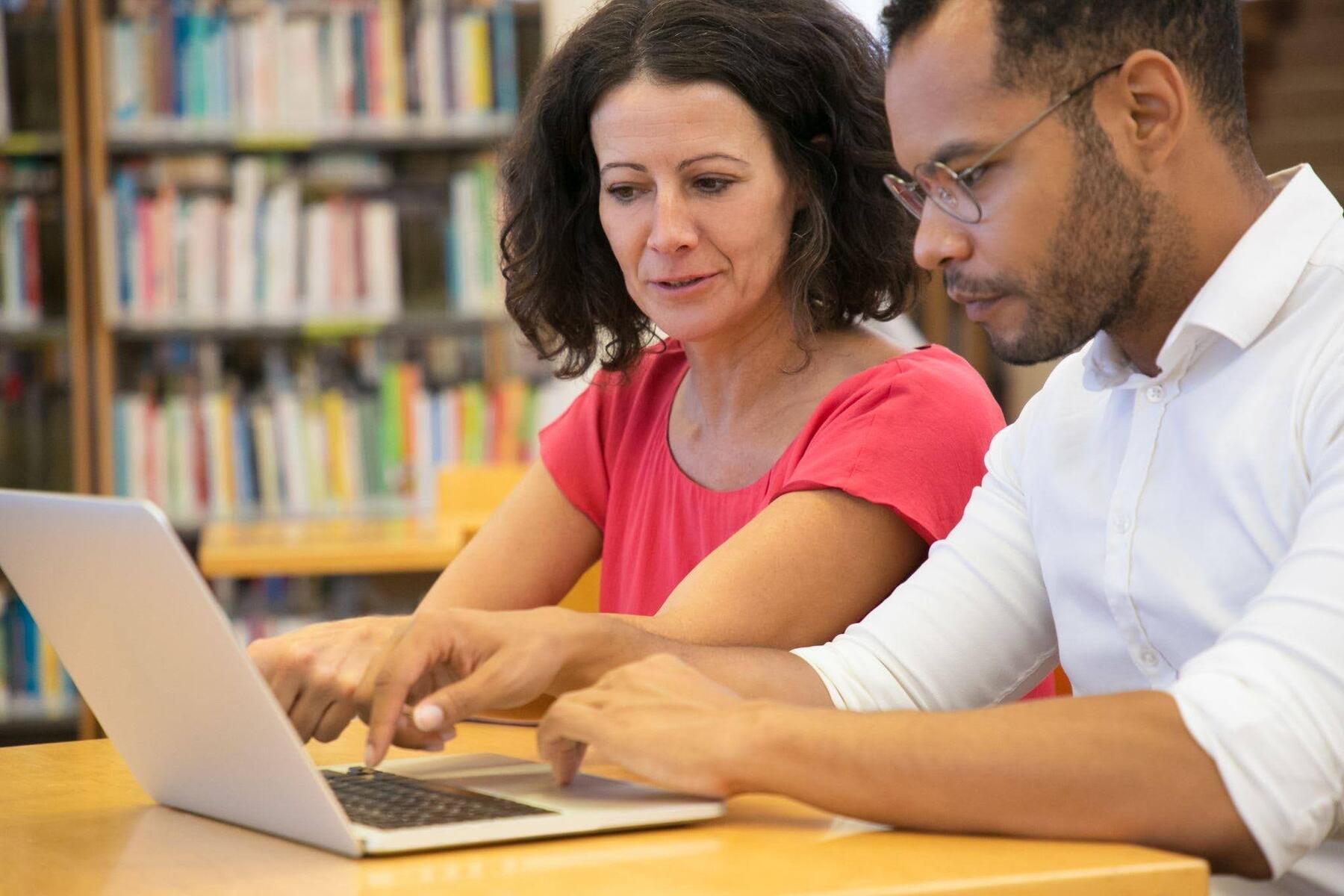 Dois estudantes analisando informações no notebook e tirando dúvidas sobre pós-graduação lato sensu e stricto sensu.