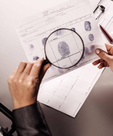 Perito criminal analisando impressões digitais com uma lupa durante a investigação de evidências.