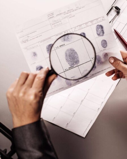 Perito criminal analisando impressões digitais com uma lupa durante a investigação de evidências.