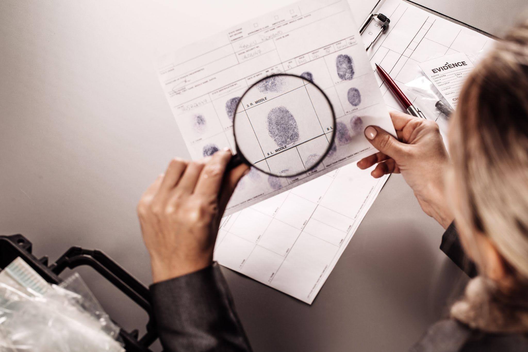 Perito criminal analisando impressões digitais com uma lupa durante a investigação de evidências.