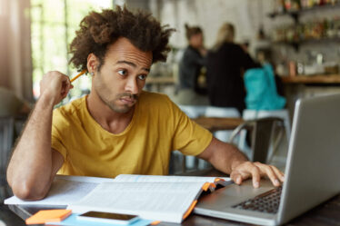 Homem estudando com livro, lápis e notebook em um ambiente acadêmico, buscando informações sobre pós-graduação reconhecida pelo MEC.