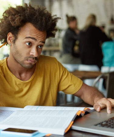 Homem estudando com livro, lápis e notebook em um ambiente acadêmico, buscando informações sobre pós-graduação reconhecida pelo MEC.