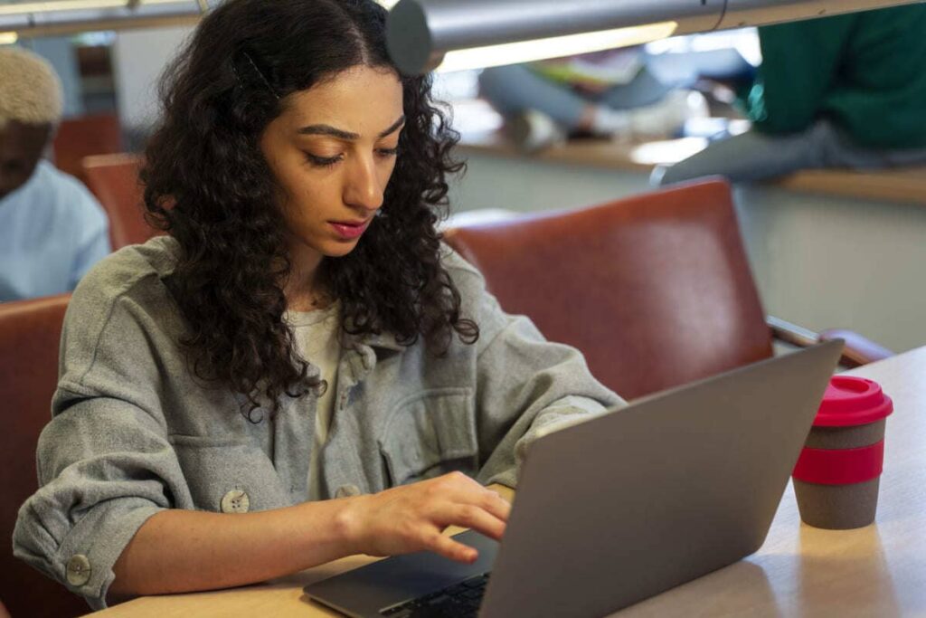 Estudante utilizando notebook em ambiente universitário, dedicada aos estudos de uma pós-graduação reconhecida pelo MEC.