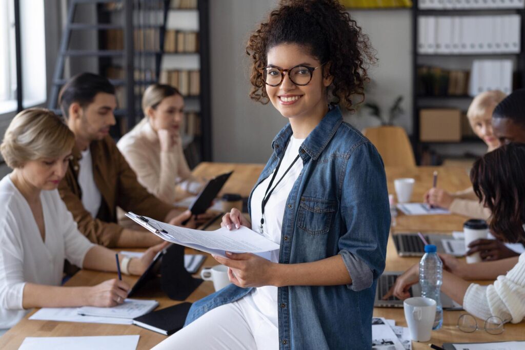 Mulher sorrindo em sala de aula com outros alunos ao fundo, ilustrando a diferença entre curso técnico e profissionalizante em ambientes educacionais.