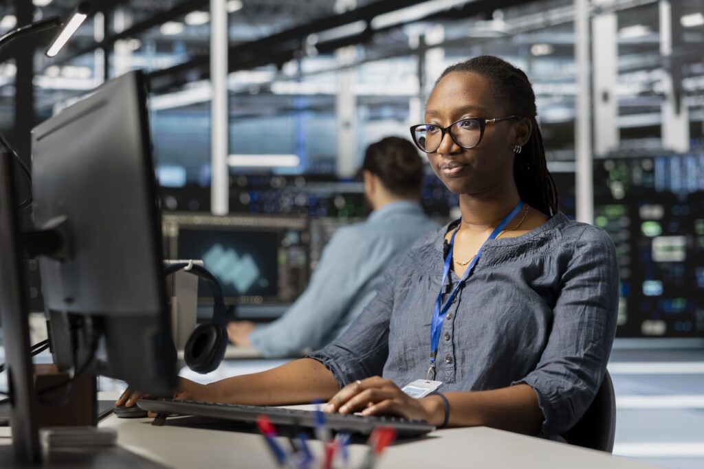 Profissional de TI analisando dados e sistemas em ambiente de data center, monitorando informações em múltiplas telas.