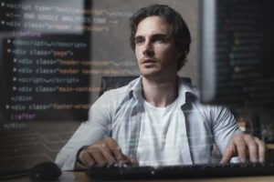 Profissional de TI programando em computador com códigos na tela, focado no desenvolvimento de software.
