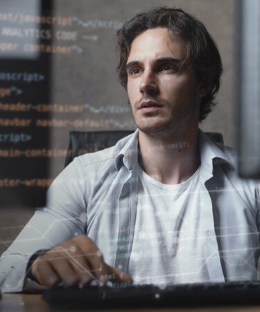 Profissional de TI programando em computador com códigos na tela, focado no desenvolvimento de software.