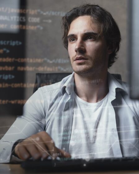 Profissional de TI programando em computador com códigos na tela, focado no desenvolvimento de software.
