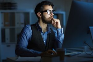 Profissional de TI trabalhando à noite em frente ao computador, concentrado em atividades de tecnologia e programação.