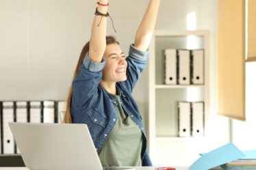 Retrato de uma jovem estagiária satisfeita levantando braços no escritório.