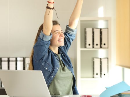 Retrato de uma jovem estagiária satisfeita levantando braços no escritório.