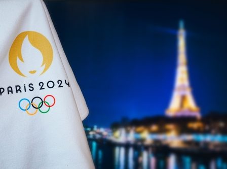 Bandeira com a escrita "PARIS 2024" e com o logo dos jogos olímpicos com a torre Eiffel ao fundo
