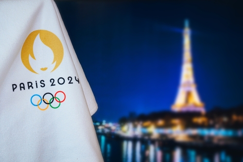 Bandeira com a escrita "PARIS 2024" e com o logo dos jogos olímpicos com a torre Eiffel ao fundo