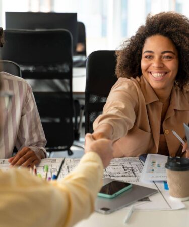 Jovem profissional celebra oportunidade de primeiro emprego ao cumprimentar recrutador durante reunião em ambiente de trabalho.