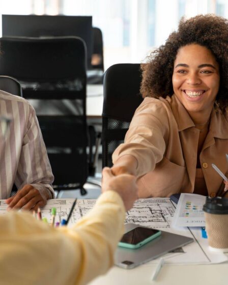 Jovem profissional celebra oportunidade de primeiro emprego ao cumprimentar recrutador durante reunião em ambiente de trabalho.