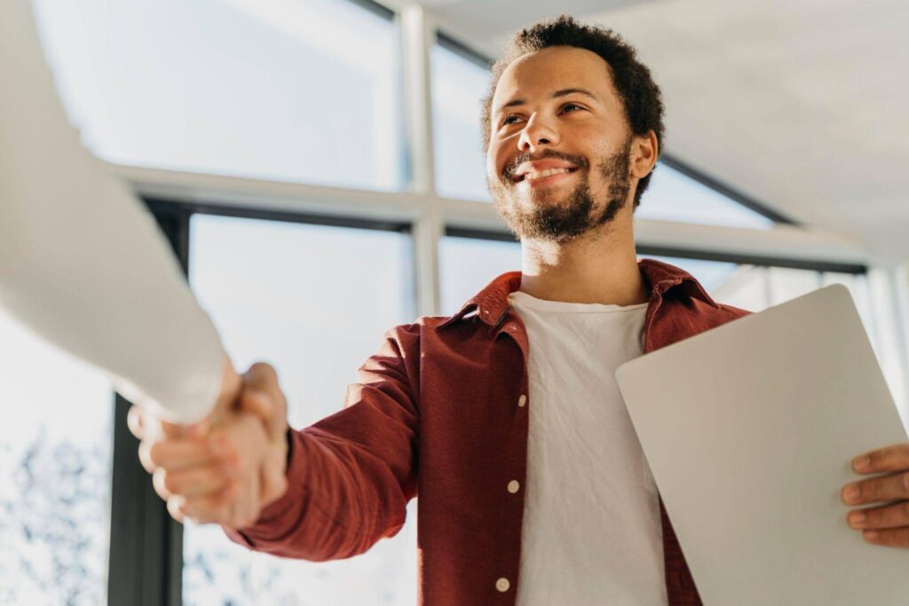 Jovem conquista o primeiro emprego após processo seletivo e aperta a mão do recrutador durante a contratação.