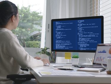 Jovem mulher cientista de dados olha para a tela do computador em que desenvolve projeto de inteligência artificial.