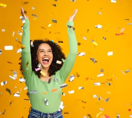 Imagem de uma mulher animada comemorando uma grande vitória, com confetes em fundo amarelo.
