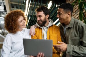 Três colegas sorrindo com notebook, representando jovens no mercado de trabalho.