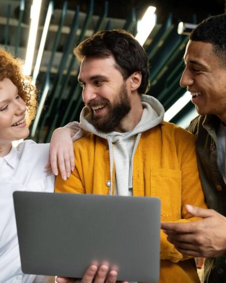 Três colegas sorrindo com notebook, representando jovens no mercado de trabalho.