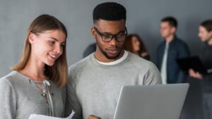 Dois profissionais analisando informações em um notebook, ilustrando jovens no mercado de trabalho em um contexto corporativo.