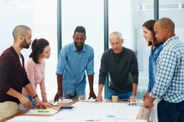 Imagem de um grupo de pessoas ao redor de uma mesa representando uma entrevista coletiva ou dinâmica em grupo.