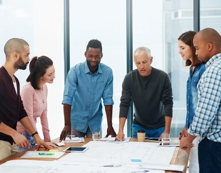 Imagem de um grupo de pessoas ao redor de uma mesa representando uma entrevista coletiva ou dinâmica em grupo.