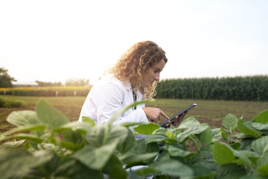 Mulher agrônoma analisando plantas com tablet em lavouras, ilustrando a carreira em Agronomia com uso de tecnologia.