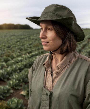 Profissional no campo de cultivo observando plantação, simbolizando a carreira em Agronomia e o trabalho diário na agricultura.