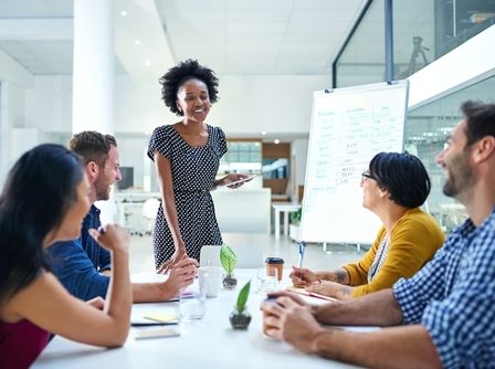 Empreendedora jovem, com semblante feliz, realizando apresentação para a sua equipe.