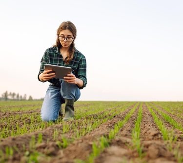 Agricultora em um campo aberto, analisando qualidade do solo em um tablet.