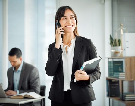 Dois juristas com roupas sociais, trabalhando em um escritório, um homem ao computador e uma mulher ao celular.