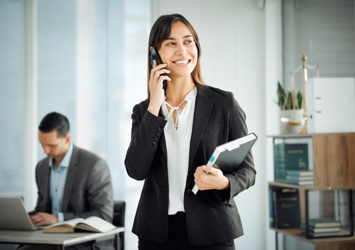 Dois juristas com roupas sociais, trabalhando em um escritório, um homem ao computador e uma mulher ao celular.