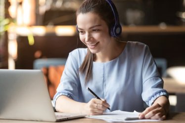 Estudante sorridente usando fones de ouvido sem fio em ambiente de estudo.