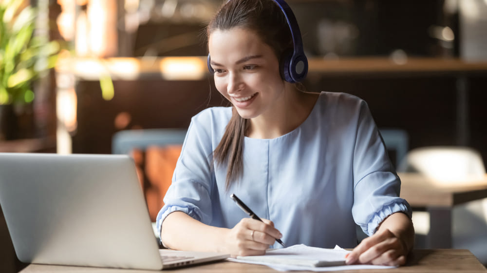 Estudante sorridente usando fones de ouvido sem fio em ambiente de estudo.