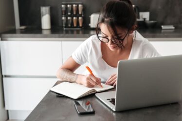 Mulher estudando com notebook e fazendo anotações em um caderno
