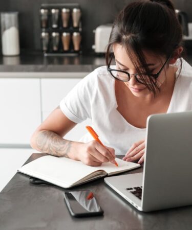 Mulher estudando com notebook e fazendo anotações em um caderno