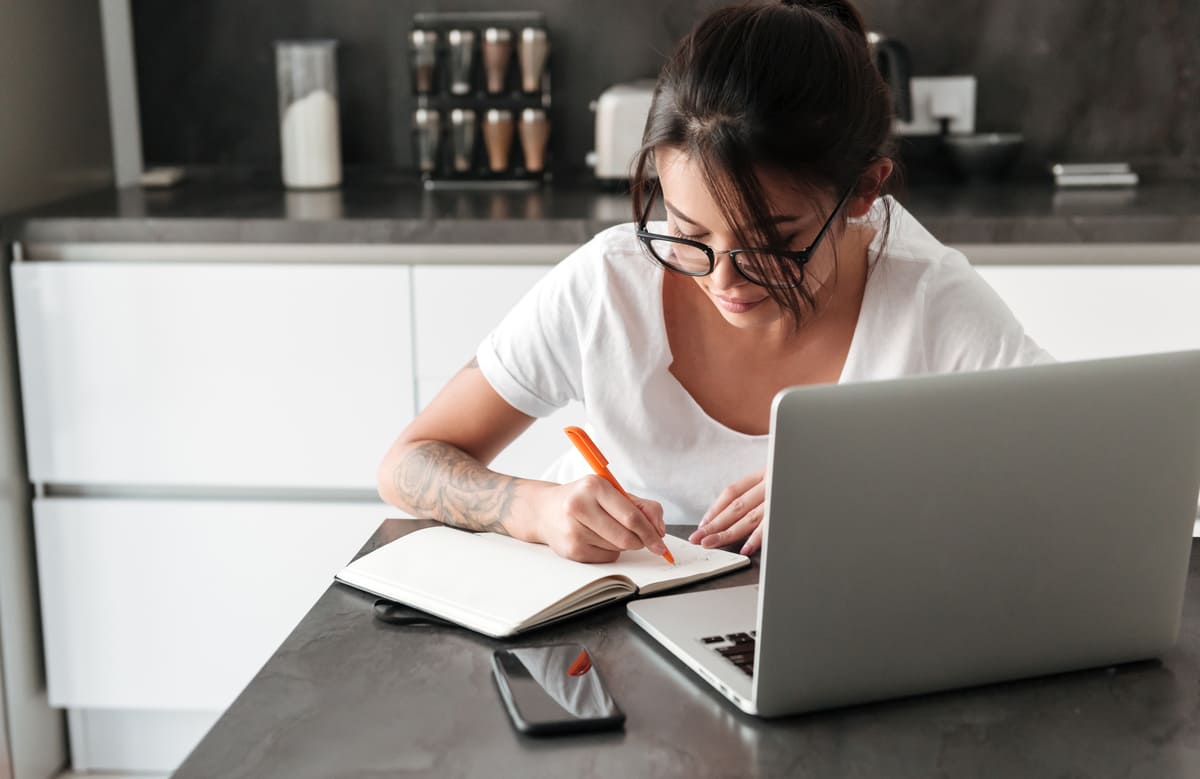 Mulher estudando com notebook e fazendo anotações em um caderno