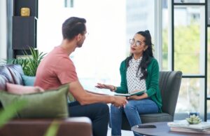 Uma mulher jovem psicóloga atendendo em seu escritório um homem jovem, em ambiente iluminado e harmonioso.