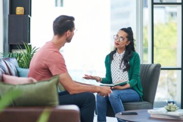 Uma mulher jovem psicóloga atendendo em seu escritório um homem jovem, em ambiente iluminado e harmonioso.