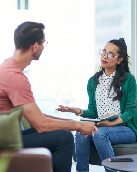 Uma mulher jovem psicóloga atendendo em seu escritório um homem jovem, em ambiente iluminado e harmonioso.