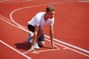 Atleta em largada de corrida em pista olímpica, pronto para competir durante evento esportivo.