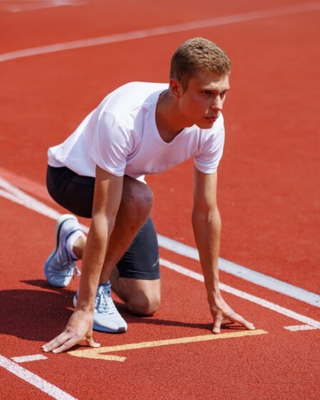 Atleta em largada de corrida em pista olímpica, pronto para competir durante evento esportivo.