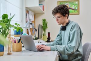 jovem estudante universitário sentado em uma mesa, estudando com laptop em uma sala de estudos.