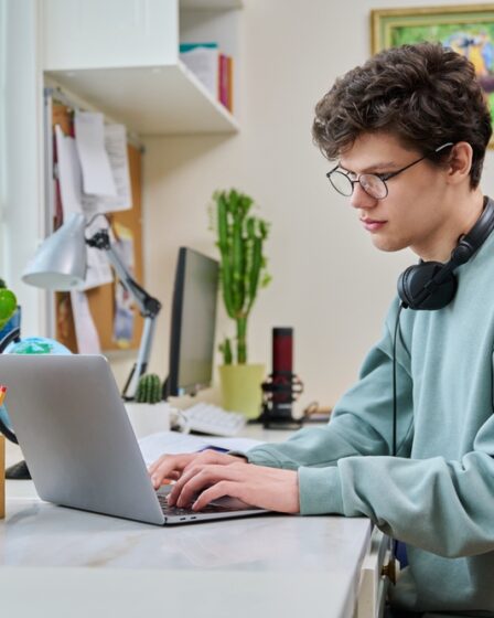 jovem estudante universitário sentado em uma mesa, estudando com laptop em uma sala de estudos.