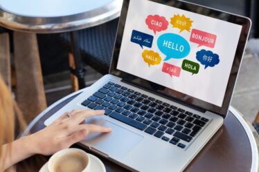 Mulher mexe em notebook em que na tela aparece formas de falar olá em diferentes línguas.
