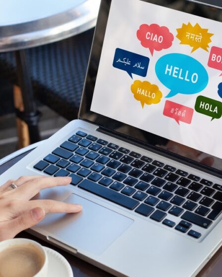 Mulher mexe em notebook em que na tela aparece formas de falar olá em diferentes línguas.